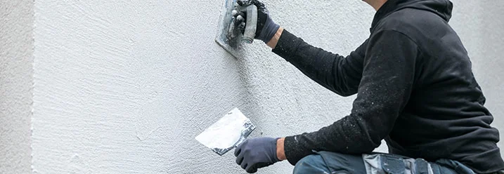 Person verputzt Fassade mit Kelle